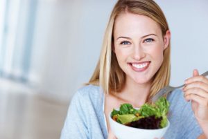 Mulher sorrindo e comendo salada | Os benefícios da alimentação saudável para a pele