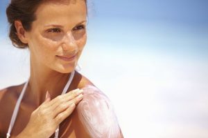 Mulher na praia passando protetor | Como evitar o câncer de pele?